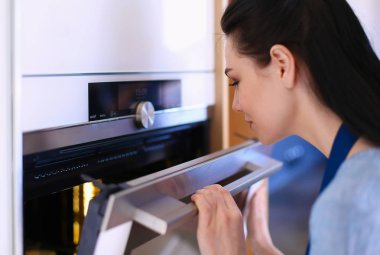 Güzel genç bayan pastasının fırında ne yaptığını kontrol ediyor.