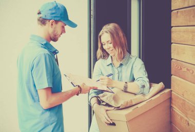 Mavi üniformalı gülümseyen kurye servis konseptine paket kutusu teslim eden teslimatçı.