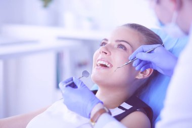 Dişçi muayenehanesinde diş muayenesi yapan ağzı açık genç bir kadın hasta..