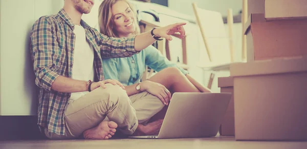 Unga par som flyttar i nya hem. Sitter på golvet och avkopplande efter uppackning. Ser något på laptop — Stockfoto