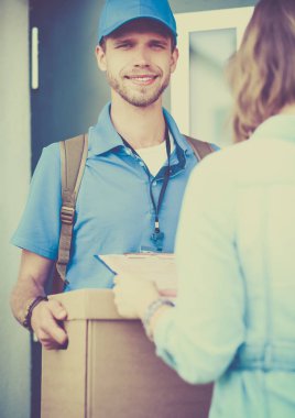 Mavi üniformalı gülümseyen kurye servis konseptine paket kutusu teslim eden teslimatçı.