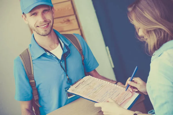 Uomo di consegna sorridente in uniforme blu che consegna pacchi al destinatario - concetto di servizio di corriere — Foto Stock