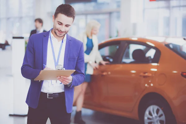 Vendedor fica perto de um carro novo no showroom — Fotografia de Stock