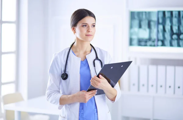 Junge lächelnde Ärztin mit Stethoskop hält im Sprechzimmer eines Krankenhauses einen Ordner in der Hand — Stockfoto