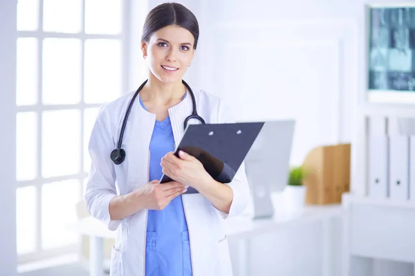 Unga leende kvinnlig läkare med stetoskop håller en mapp på ett sjukhus konsultrum — Stockfoto
