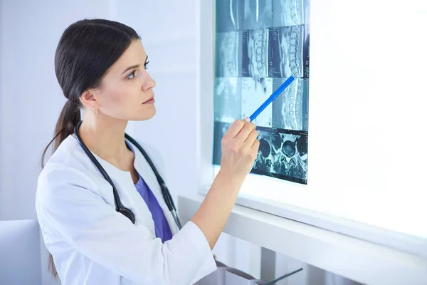 Young smiling female doctor with stethoscope pointing at X-ray at doctors office — Stock Photo, Image