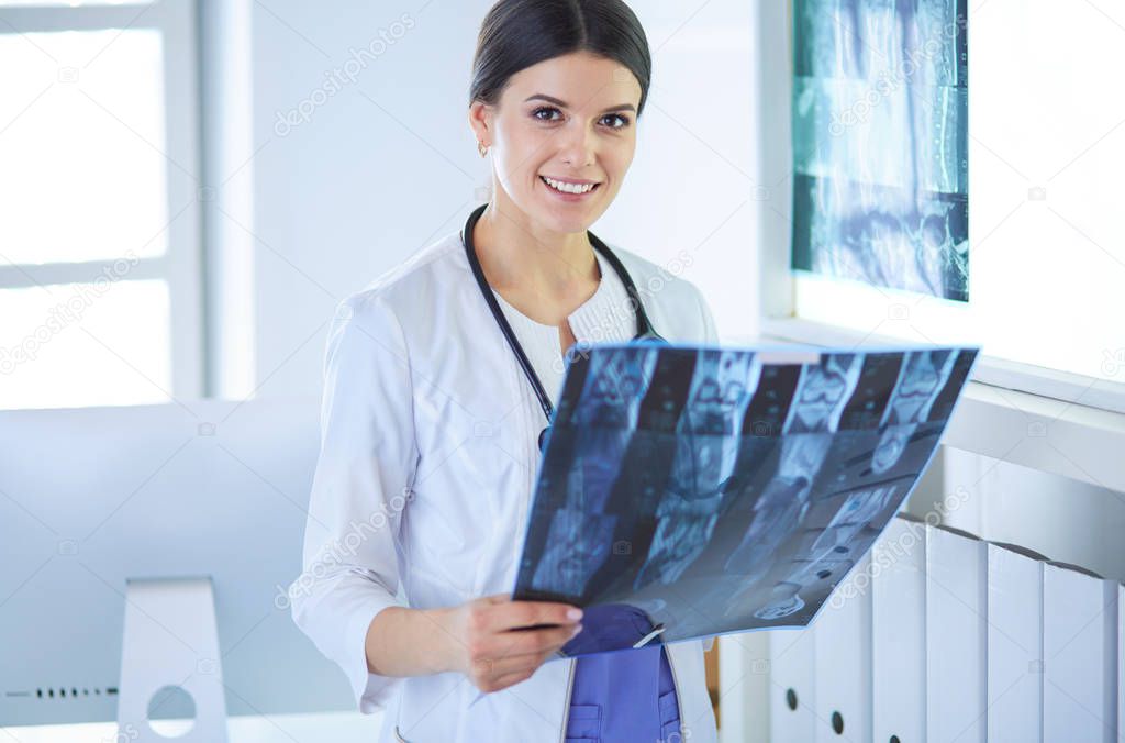 Young female doctor with stethoscope examining X-ray at doctors office
