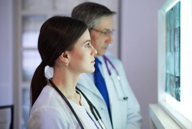 Bir grup doktor bir klinikte röntgenleri inceliyor, teşhis koymayı düşünüyorlar.