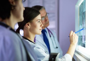 Bir grup doktor bir klinikte röntgenleri inceliyor, teşhis koymayı düşünüyorlar.