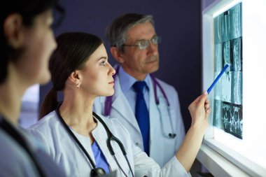 Bir grup doktor bir klinikte röntgenleri inceliyor, teşhis koymayı düşünüyorlar.