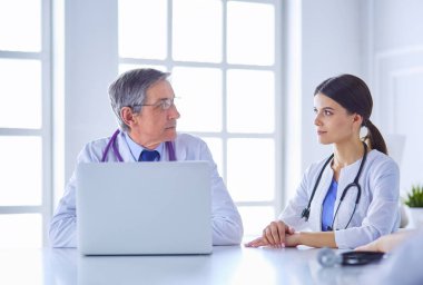 Ciddi bir tıbbi ekip, parlak bir danışma odasında dizüstü bilgisayar kullanıyor.