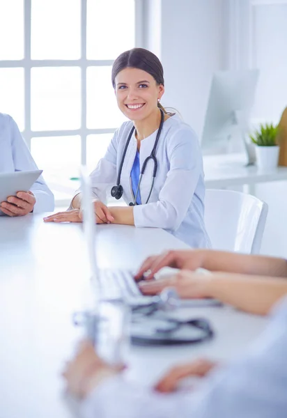 Lachende arts met behulp van een laptop werken met haar collega 's in een heldere ziekenhuiskamer — Stockfoto