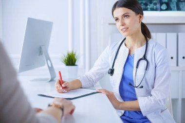 Doktor ve hasta hastane danışma odasında tıbbi sorunları tartışıyorlar. Doktor hasta formunu dolduruyor.
