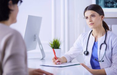 Doktor ve hasta hastane danışma odasında tıbbi sorunları tartışıyorlar. Doktor hasta formunu dolduruyor.