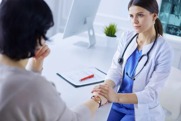 Vrouwelijke dokter kalmeert een patiënt in een ziekenhuis spreekkamer, houdt haar hand vast — Stockfoto