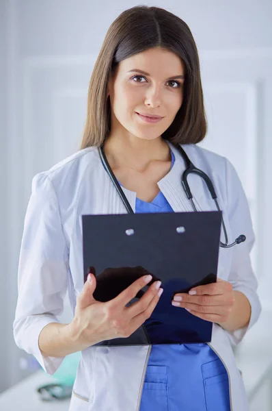 Ženská doktorka stojí se složkou v ruce v nemocnici a usmívá se do kamery — Stock fotografie
