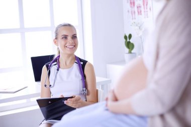 Steteskoplu ve tabletli genç kadın doktor hastanede hamile bir kadınla konuşuyor..