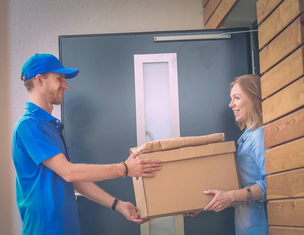 Mavi üniformalı gülümseyen kurye servis konseptine paket kutusu teslim eden teslimatçı. Mavi üniformalı gülümseyen teslimatçı.