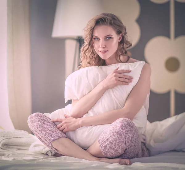 Young woman holding a pillow while sitting on her bed. — Stock Photo, Image