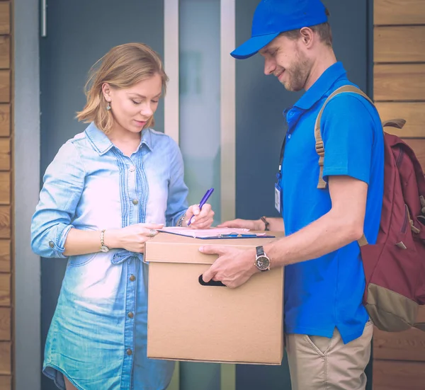 Repartidor sonriente con uniforme azul que entrega la caja de paquetes al destinatario: concepto de servicio de mensajería. Repartidor sonriente en uniforme azul — Foto de Stock