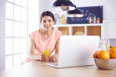 Mutfakta dizüstü bilgisayara benzeyen tariflerle gülümseyen genç bir kadın. Gıda blogcusu kavramı