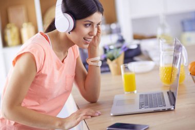 Mutfakta dizüstü bilgisayara benzeyen tariflerle gülümseyen genç bir kadın. Gıda blogcusu kavramı.