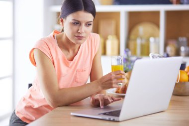 Mutfakta dizüstü bilgisayara benzeyen tariflerle gülümseyen genç bir kadın. Gıda blogcusu kavramı