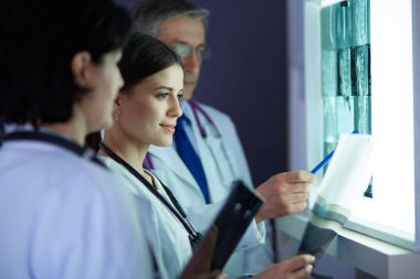 Bir grup doktor bir klinikte röntgenleri inceliyor, teşhis koymayı düşünüyorlar.