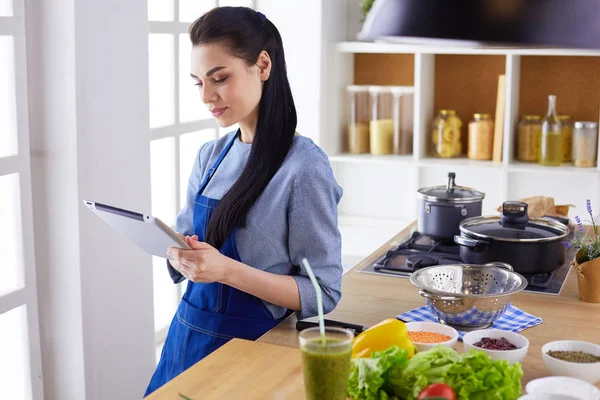 Jovem usando um computador tablet para cozinhar em sua cozinha — Fotografia de Stock