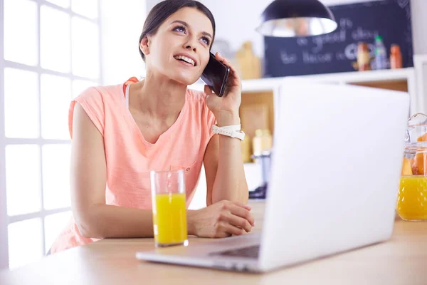 Jeune femme dans la cuisine avec ordinateur portable à la recherche de recettes, souriant. Concept de blogueur alimentaire — Photo