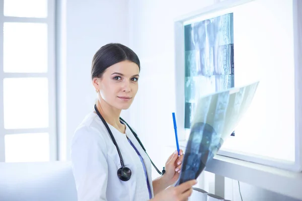 젊은 여성 의사가 청진기를 들고 웃으면서 의사 사무실에서 엑스레이를 보고 있는 모습 — 스톡 사진