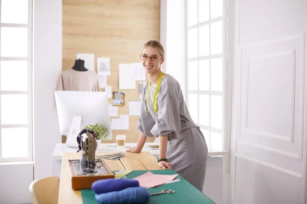 Neue modische Stile schaffen. Fröhliche junge Frau näht, während sie an ihrem Arbeitsplatz in der Modewerkstatt sitzt — Stockfoto