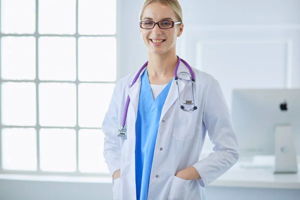 Молода жінка-лікар стоїть біля столу, ізольована на білому тлі — стокове фото