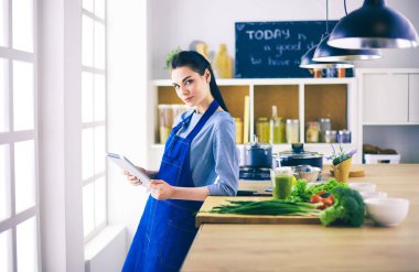 Mutfakta yemek yapmak için tablet bilgisayar kullanan genç bir kadın.