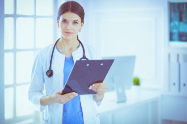 Doktor muayenehanesinde steteskopla gülümseyen genç bir bayan doktor.