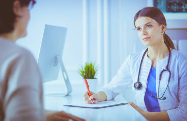 Doktor ve hasta hastane danışma odasında tıbbi sorunları tartışıyorlar. Doktor hasta formunu dolduruyor.