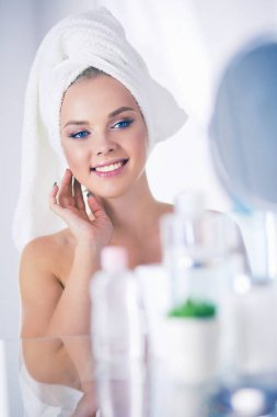 Bornozlu genç kadın banyo aynasına bakıyor.