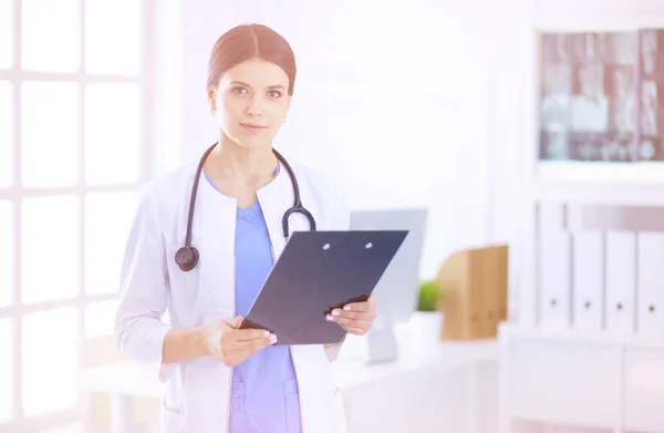 Joven doctora sonriente con estetoscopio sosteniendo una carpeta en el consultorio médico — Foto de Stock