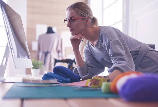 Unga attraktiva kvinnor modedesigner lutar sig mot kontorsbord, arbetar med en bärbar dator — Stockfoto