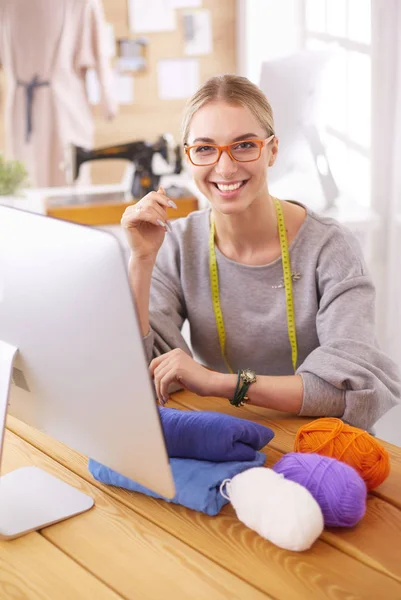 Een portret van een jonge ontwerper vrouw met behulp van een laptop en glimlachend, kleren opgehangen als achtergrond — Stockfoto