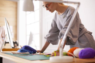 Genç çekici kadın moda tasarımcıları ofis masasına yaslanıp dizüstü bilgisayarla çalışıyorlar.