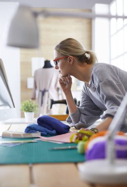 dizüstü bilgisayar ve elbise formu ile stüdyoda çalışan moda tasarımcısı