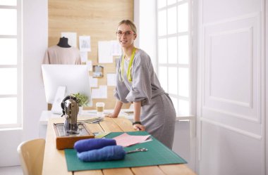 Yeni moda tarzlar yaratıyor. Moda atölyesinde çalışırken dikiş diken neşeli genç bir kadın.