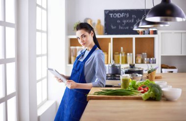 Mutfakta yemek yapmak için tablet bilgisayar kullanan genç bir kadın.