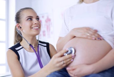 Genç bayan doktor klinikte hamile kadını muayene ediyor..