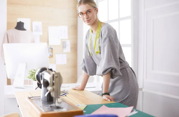 Creare nuovi stili alla moda. Allegro giovane donna cucire mentre seduto al suo posto di lavoro nel laboratorio di moda — Foto Stock