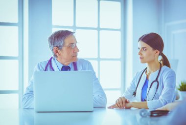 Ciddi bir tıbbi ekip, parlak bir danışma odasında dizüstü bilgisayar kullanıyor.