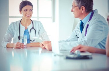 Parlak bir hastane odasında meslektaşlarıyla çalışan gülümseyen bir doktor.