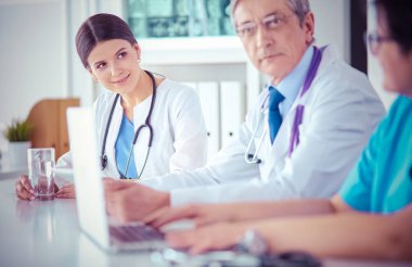 Parlak bir hastane odasında meslektaşlarıyla çalışan gülümseyen bir doktor.