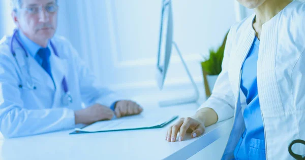 En läkare ler mot kameran med sin manliga kollega på baksidan av konsultrummet på sjukhuset — Stockfoto